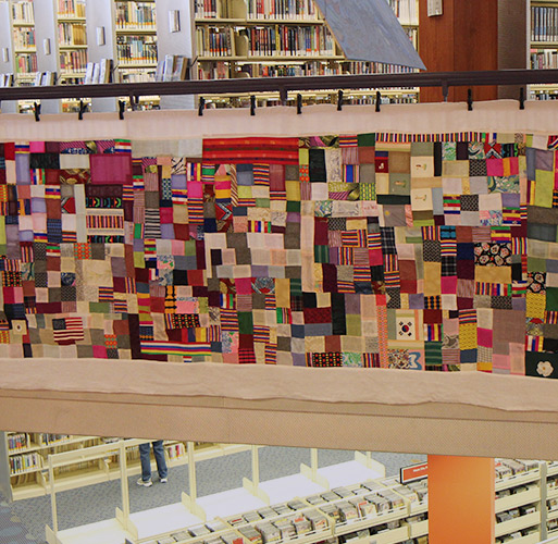 Bojagi tapestry hanging from a second floor railing with bookshelves above and CD shelving below on the first floor