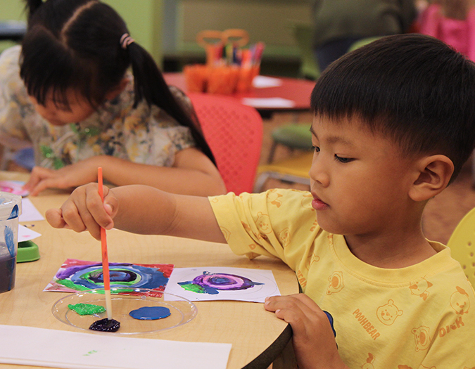 A young child grasps a paintbush during an arts program at the library