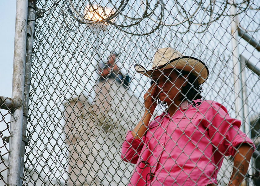 woman in pink western shirt and a cowboy hat standing behind a barbed wire-topped fence