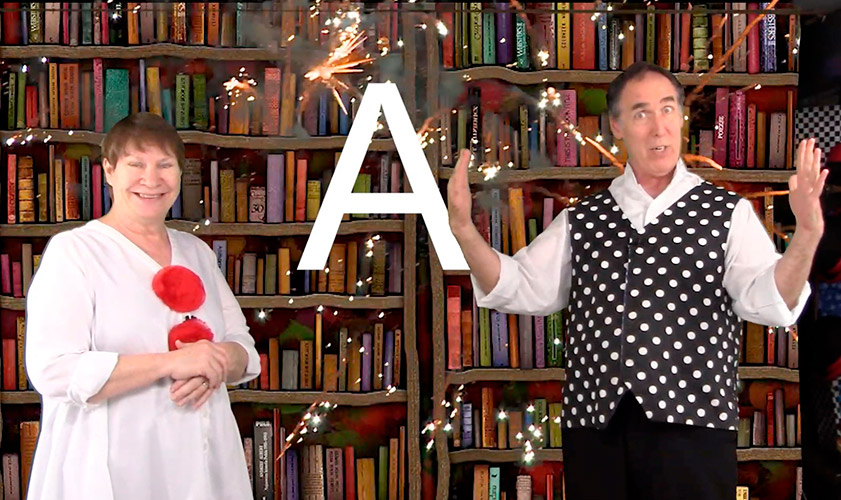 Performers Jay and Leslie Cady stand in front of a backdrop of books with a large letter "A" and sparkles of light superimposed between them