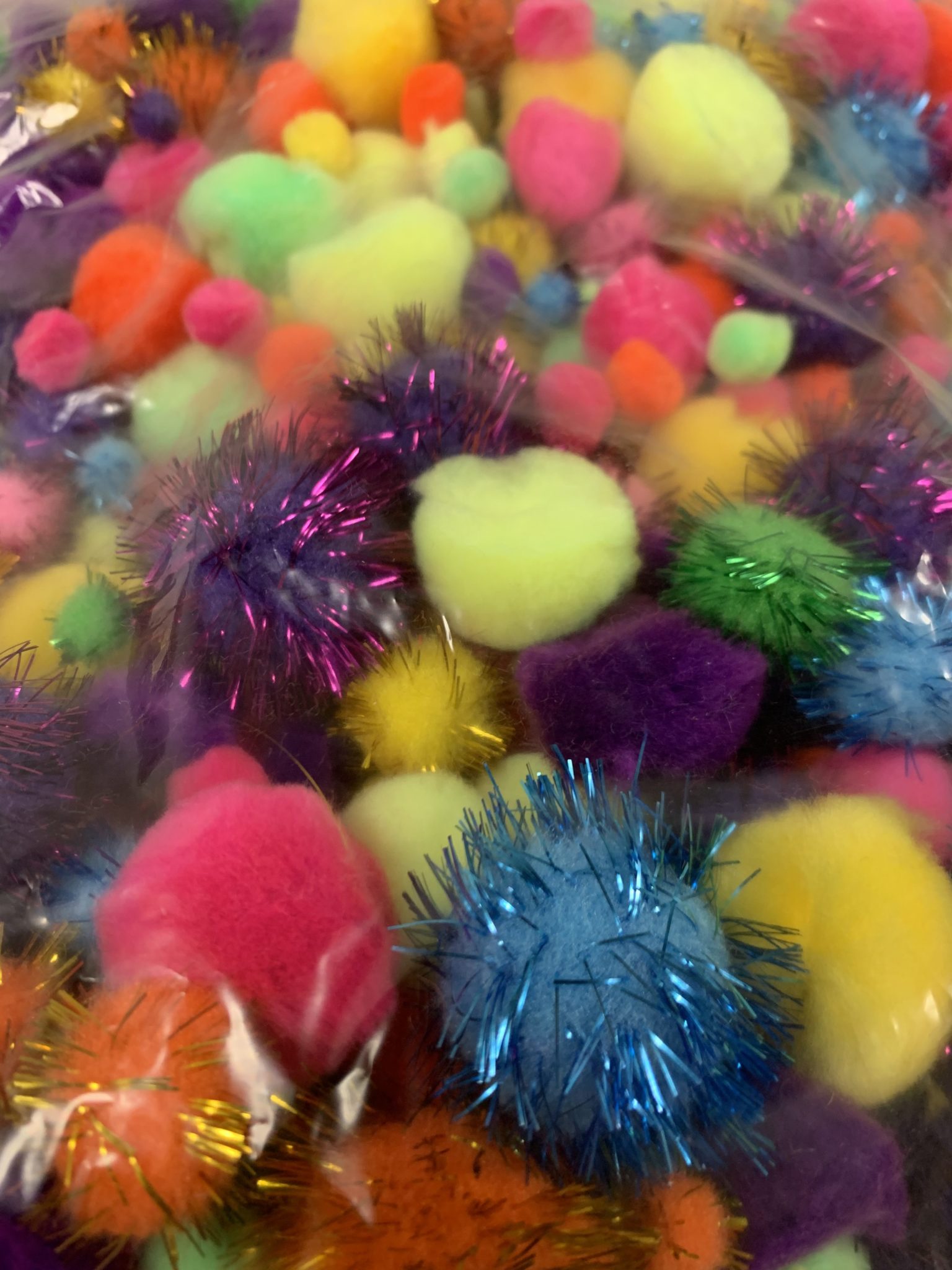 Clear plastic bag of multicolored pom-poms.