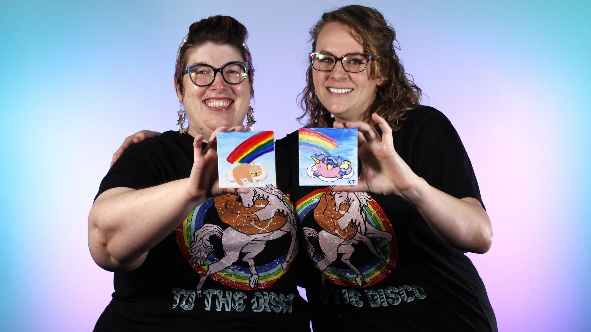 Image of Megan and Kristy holding painting of slothicorn and unicorn.