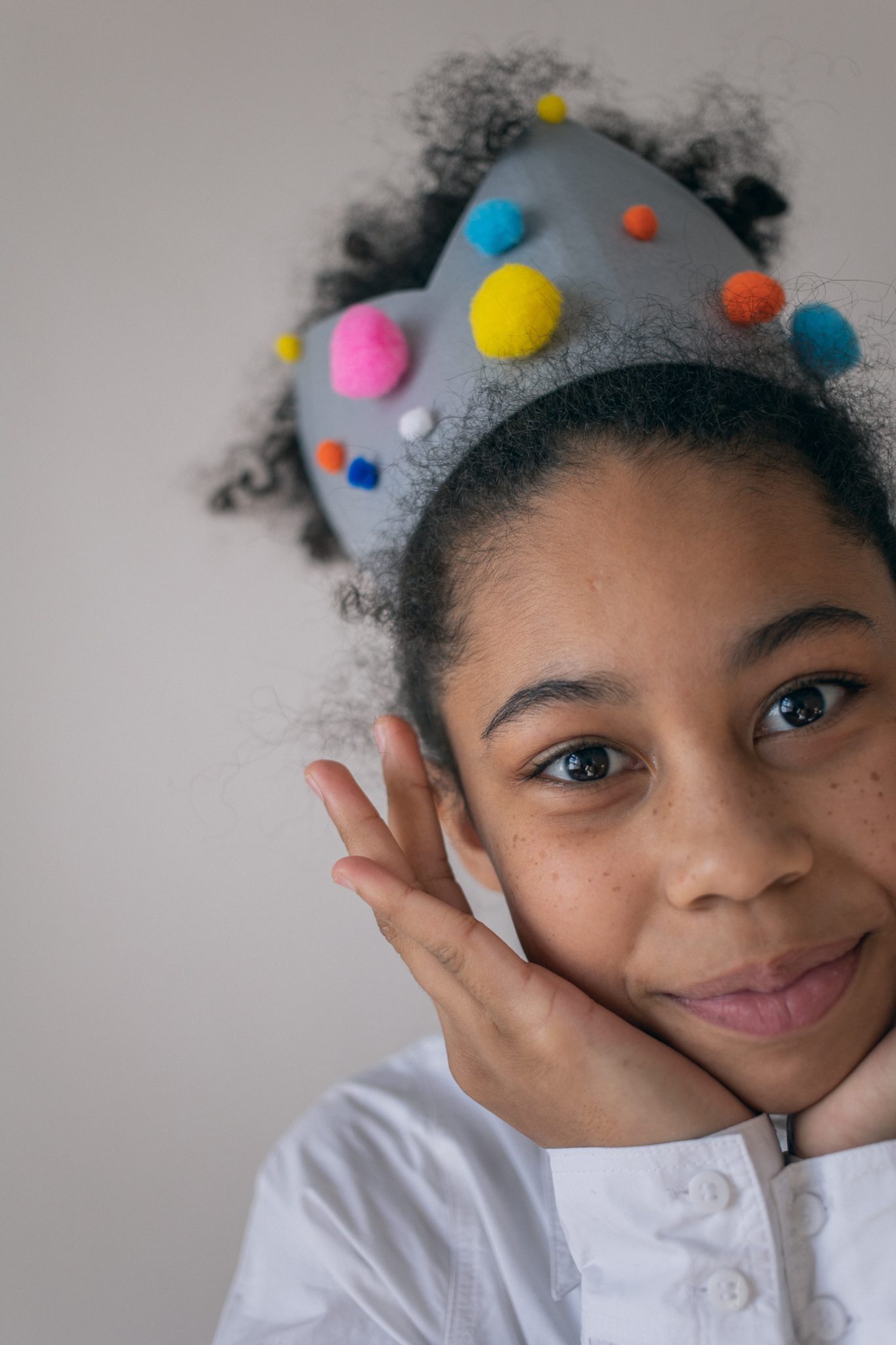 Positive black girl in creative crown touching face and smiling at camera