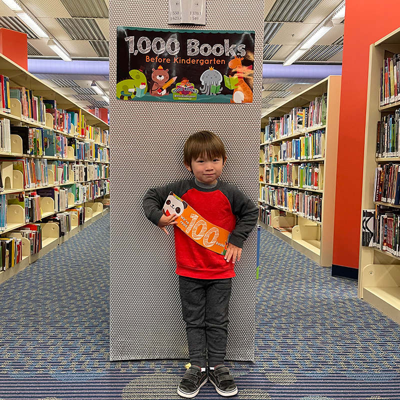 A participant in DBRL's 1,000 Books Before Kindergarten program holds up a sign reading "we've read 100 books"