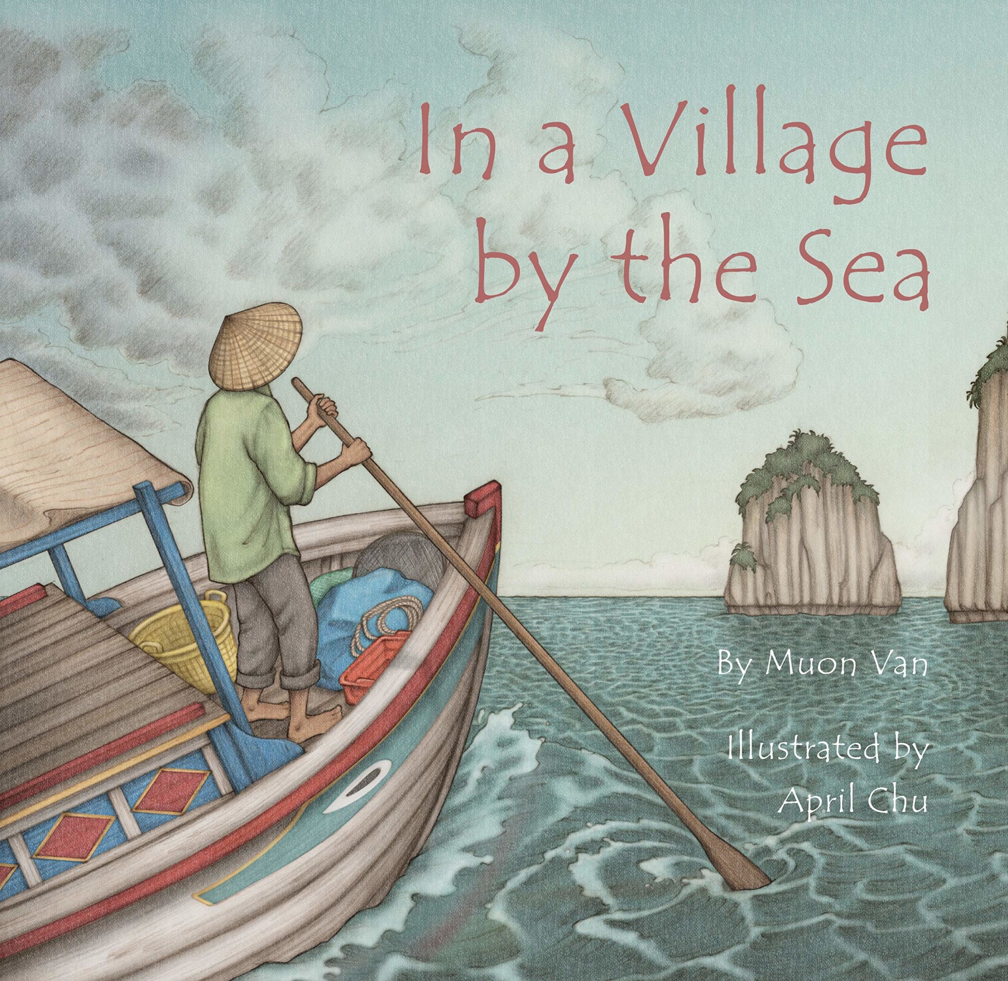 The cover of the book "In a Village by the Sea" shows a Vietnamese man in a traditional straw hat paddling his brightly-colored boat across the sea with tall cliffs in the background.