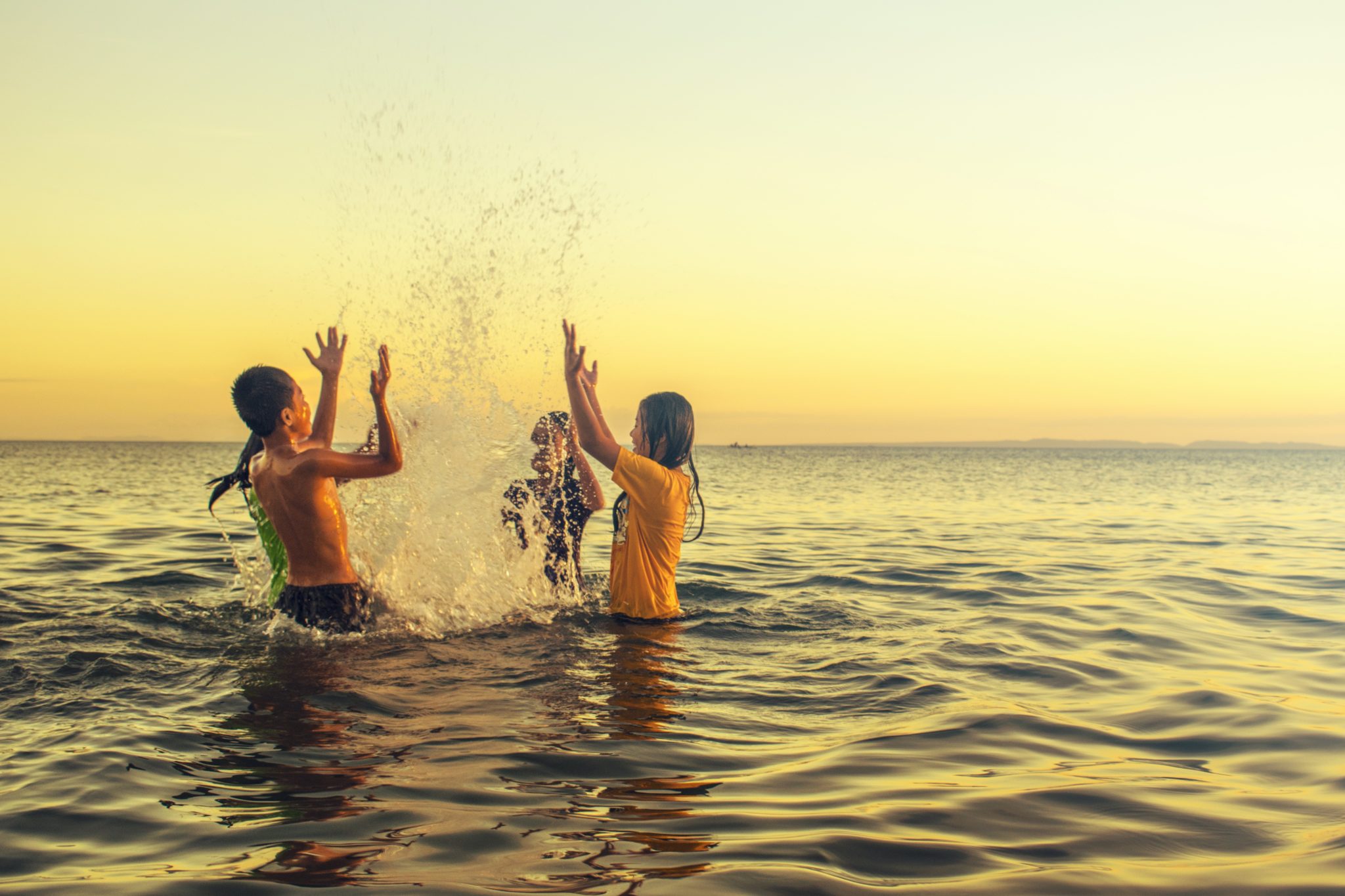 A group of children face each other in a circle and splash in the ocean water, their arms raised.