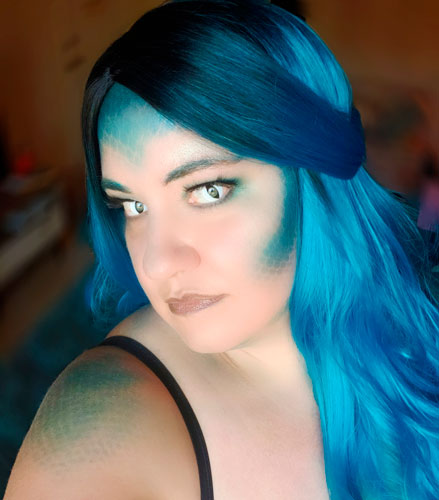 Person with long blue hair and blue scales on face and shoulders