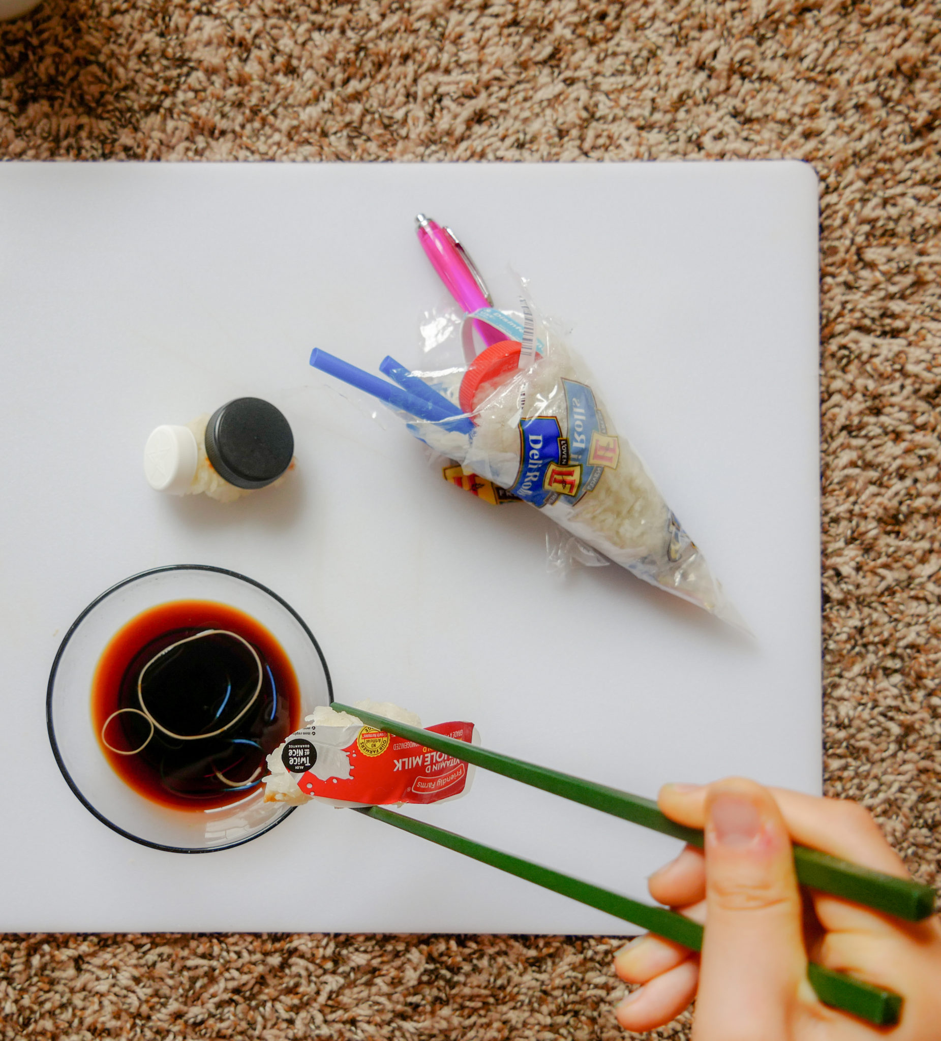 Hand holding chopsticks with sushi roll made of plastics and rice.