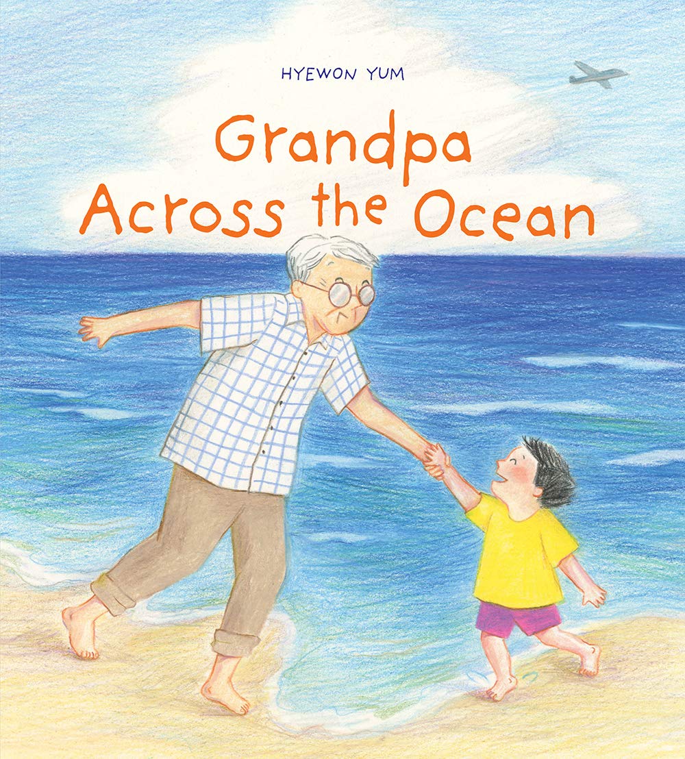 The cover of the picture book "Grandpa Across the Ocean" features a Korean grandfather and his grandson holding hands at the beach with the ocean behind them.