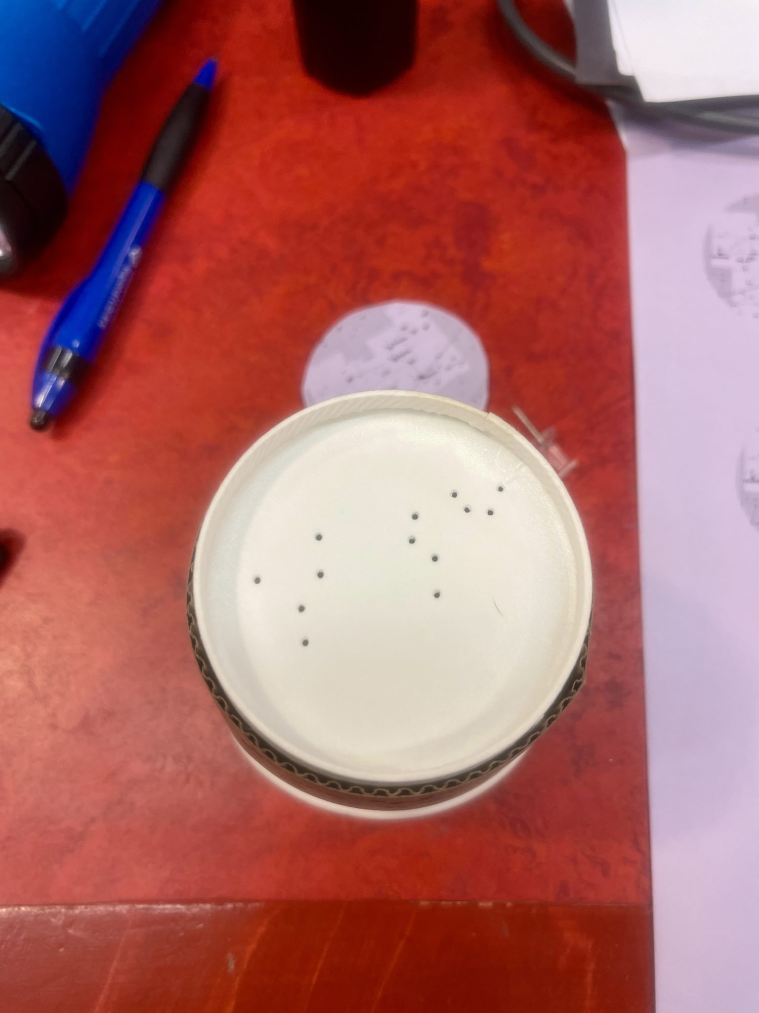 Image of a paper coffee cup turned upside down. On the bottom of the cup, a map of the constellation Leo is incised with small pinpricks.