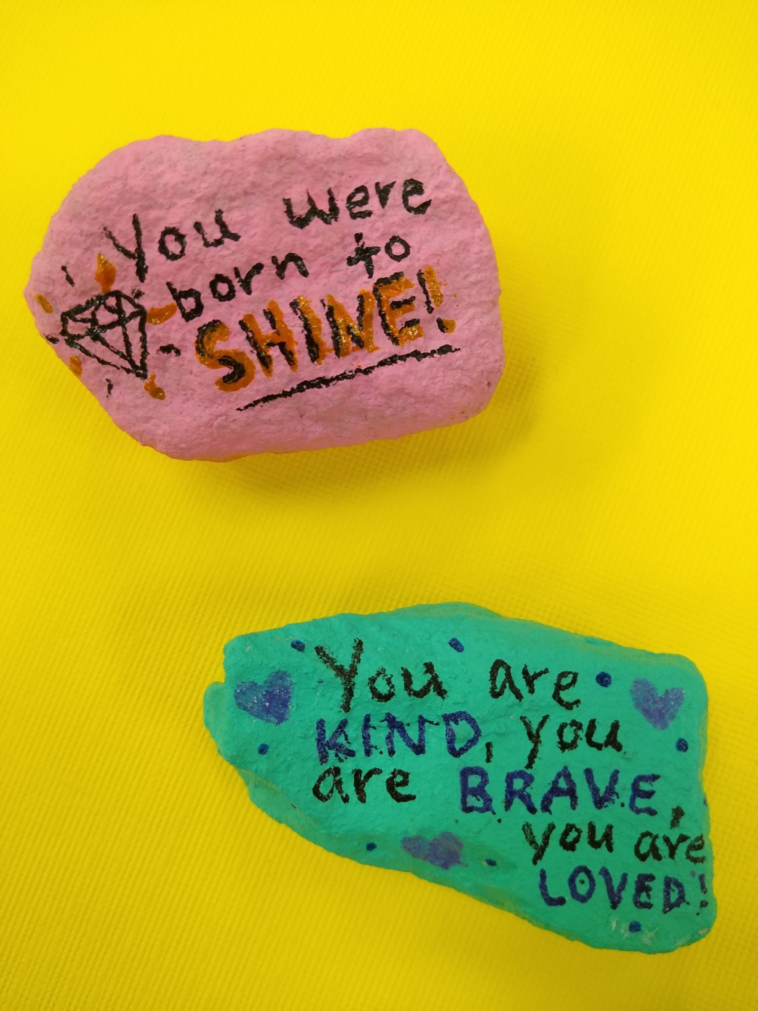 Two brightly painted rocks with the messages "You were born to shine" and "You are kind, you are brave, you are loved."