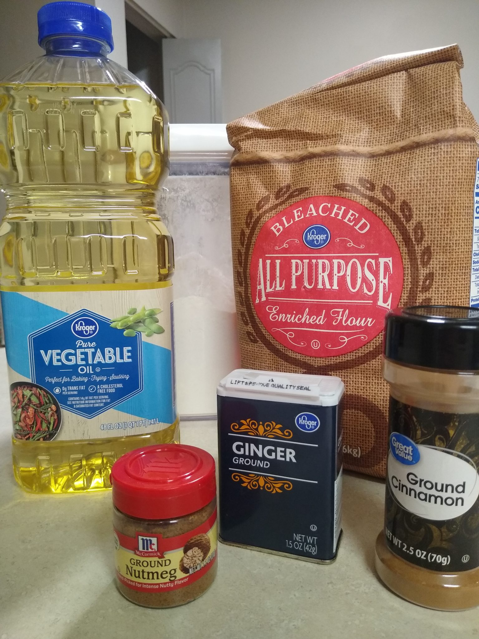 The ingredients for gingerbread dough, including vegetable oil, flour, cinnamon, nutmeg, and ginger, are displayed on a kitchen countertop. 