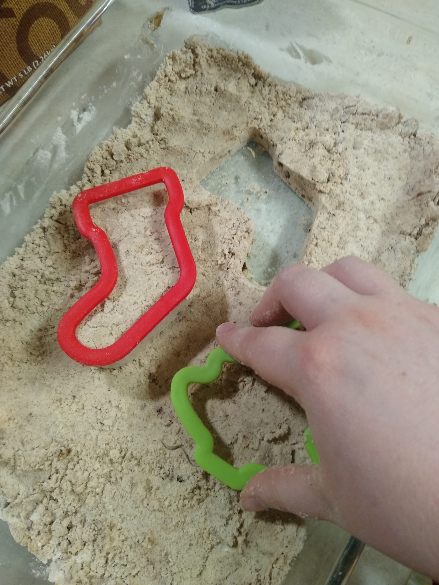 Playing in the dough using cookie cutters shaped like a stocking and a Christmas tree. 