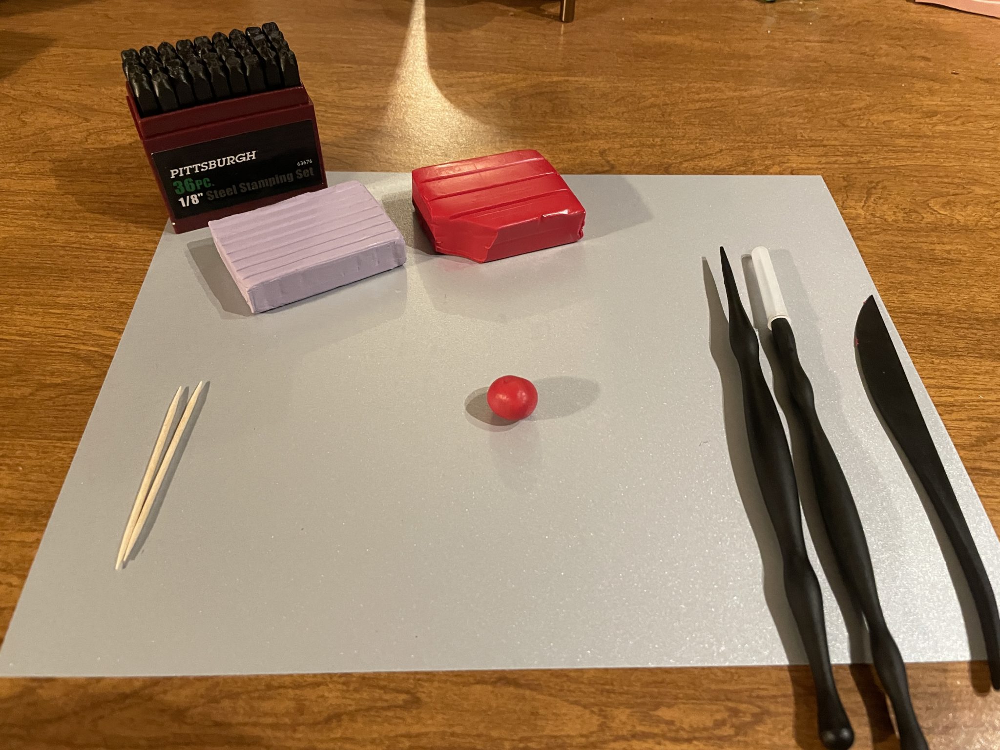 Photo of materials needed to make your own clay conversation heart. A piece of the red clay block has been torn off and rolled into a small ball. The small red clay ball is centered on the silver construction paper. 