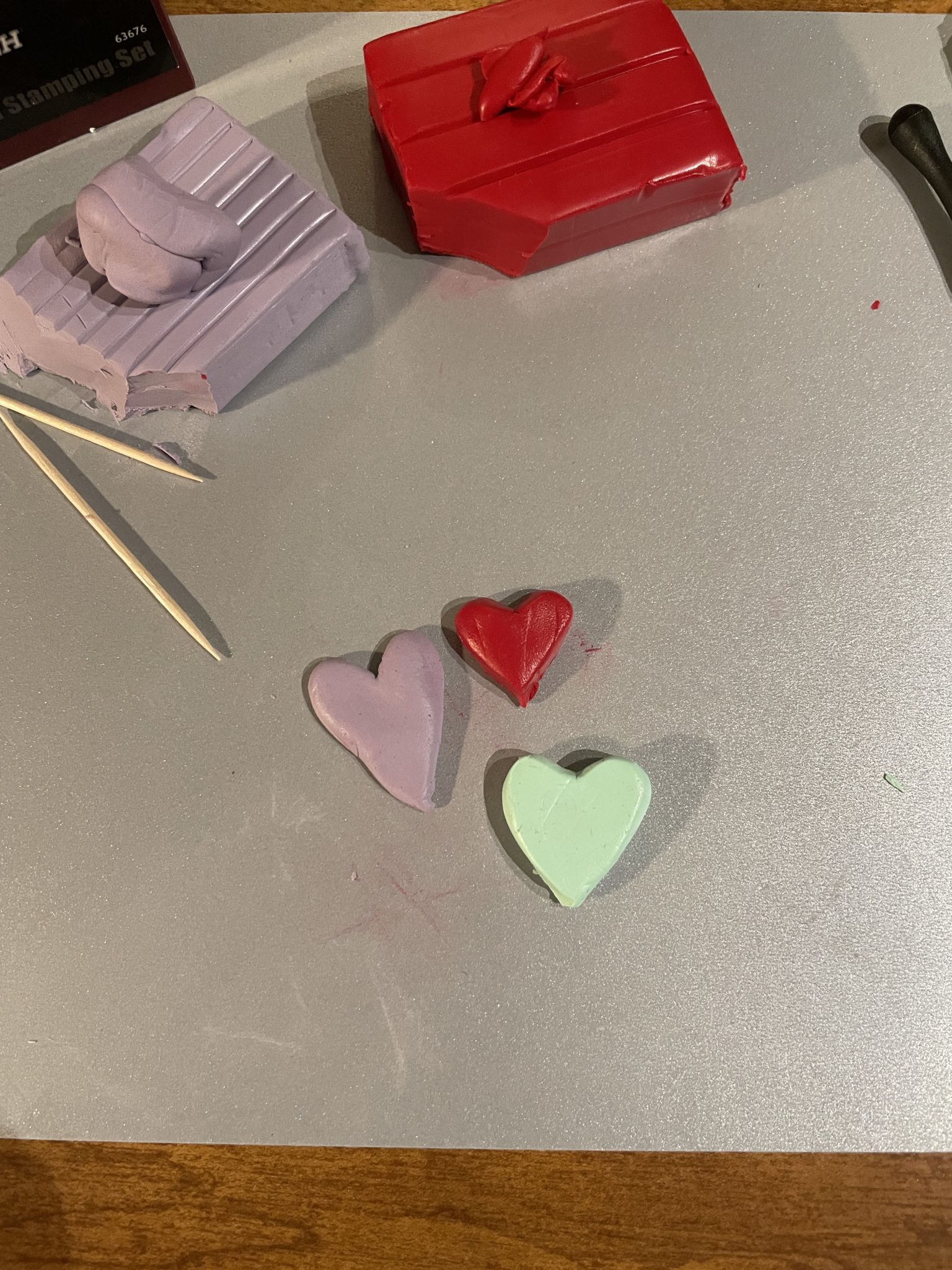 Close-up photo of three clay hearts in various sizes and colors: the smallest heart in red, the medium-sized heart in mint green, and the largest clay heart in lilac.