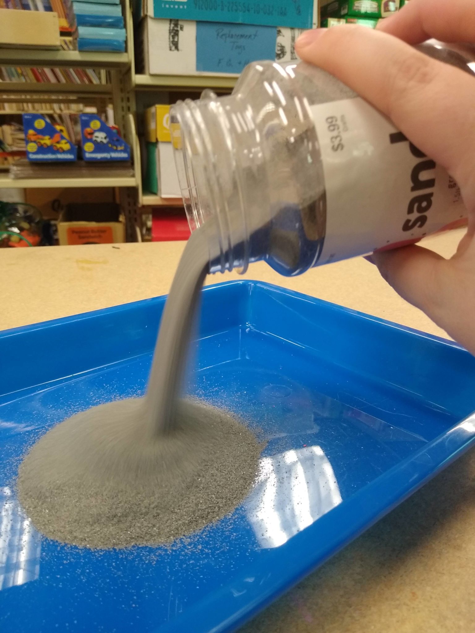 Pouring gray sand into a shallow tray.
