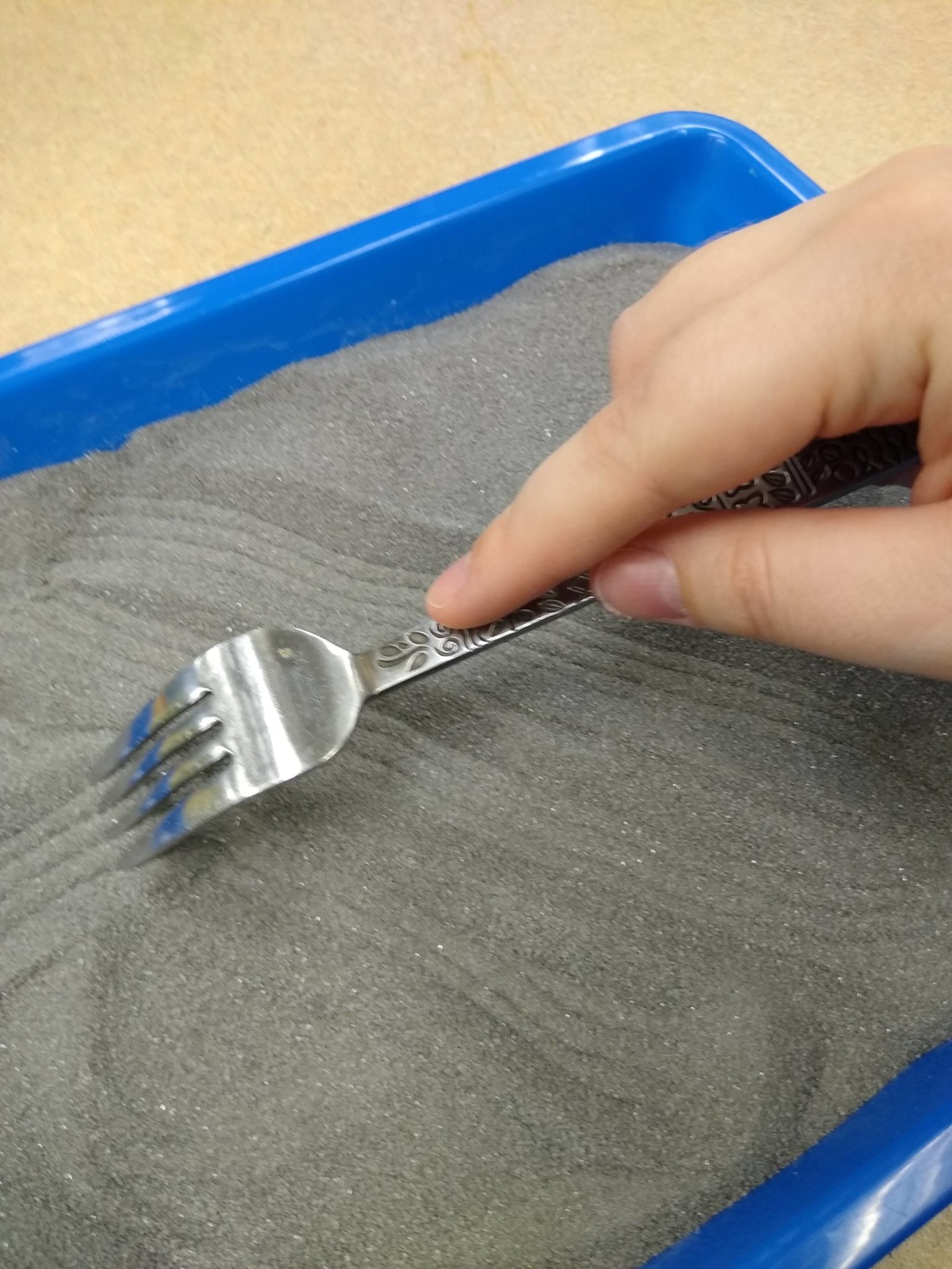 Dragging a fork through the sand to create a pattern of lines. 