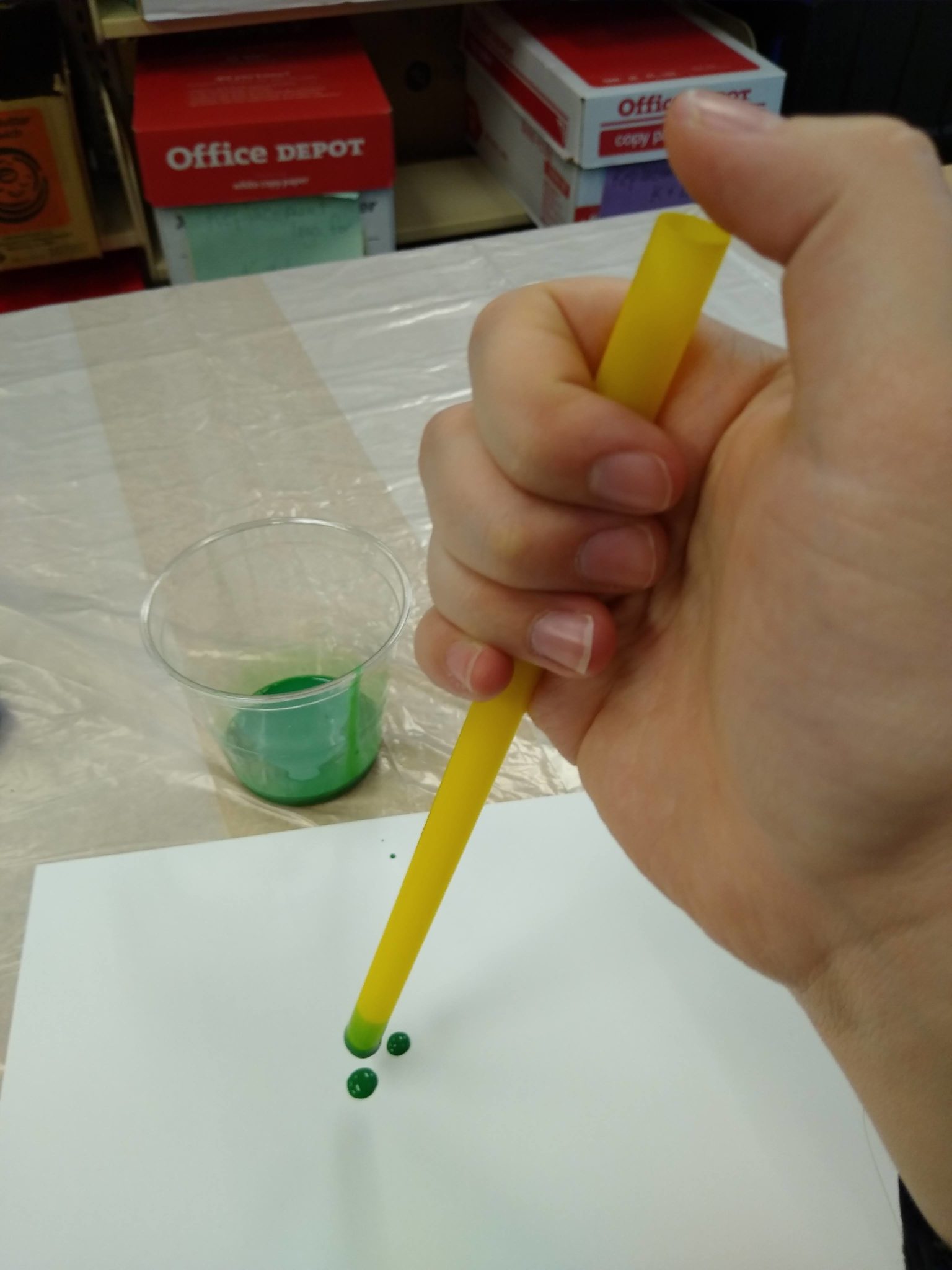 Releasing the paint by holding the straw over the paper then removing the thumb from the top of the straw.