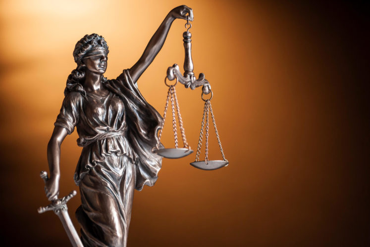 Bronze statue of Justice carrying a sword and holding up scales representing law and order over a brown background with copy space