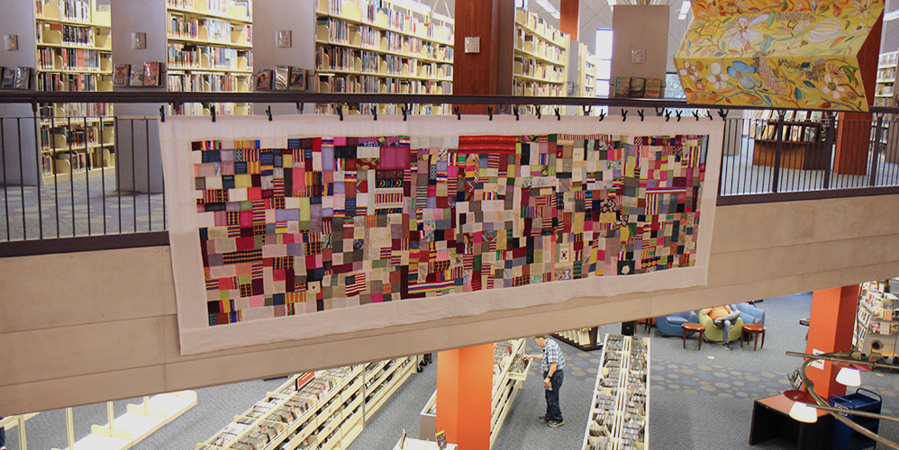 The bojagi is shown hanging from the second story railing in the library with book shelves above and CD shelving below on the first floor