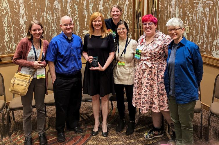 Library staff flank Lauren Williams in a posed shot as she holds her award