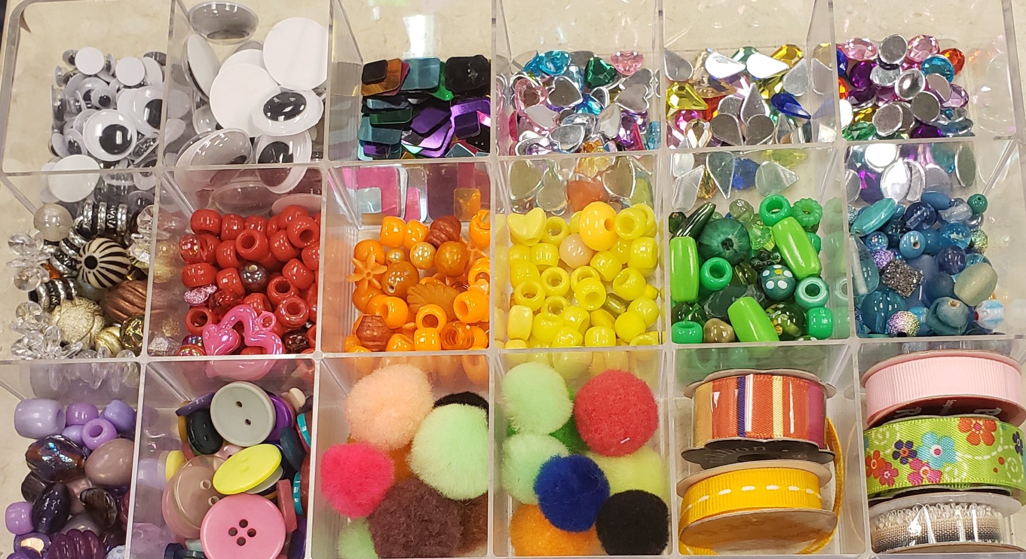 Tray with examples of loose parts: googly eyes, sequins of various sizes, beads, buttons, pom poms and ribbon.