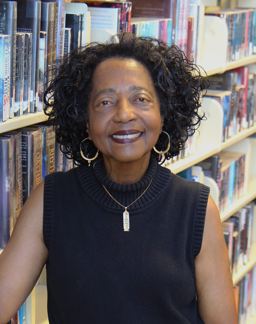 Board member Jacqueline Kelly stands in front of library book shelves