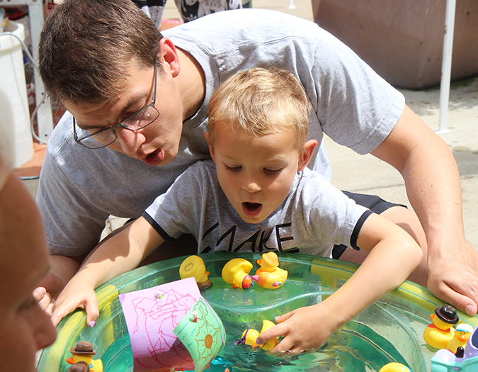 A father watches over his young child as he grasps toys floating in a small pool