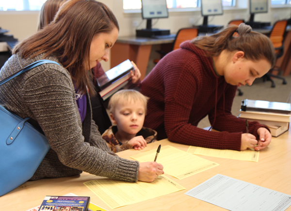 A family signs up for library cards at the Holts Summit Public Library front desk with computers in the background