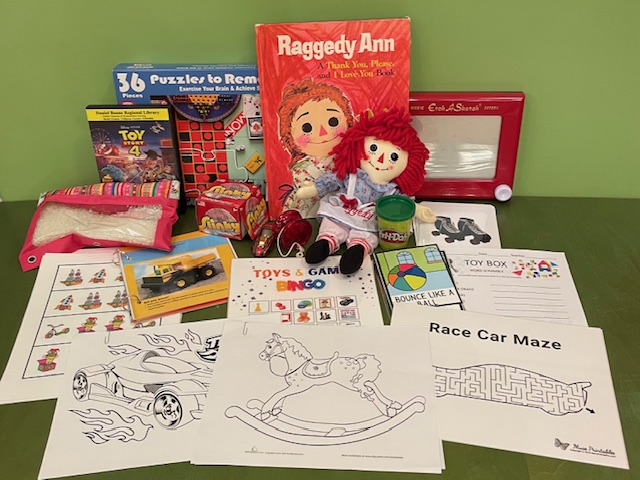 A variety of toys, books, and puzzles, including Raggedy Ann and and Etch-a-Sketch.