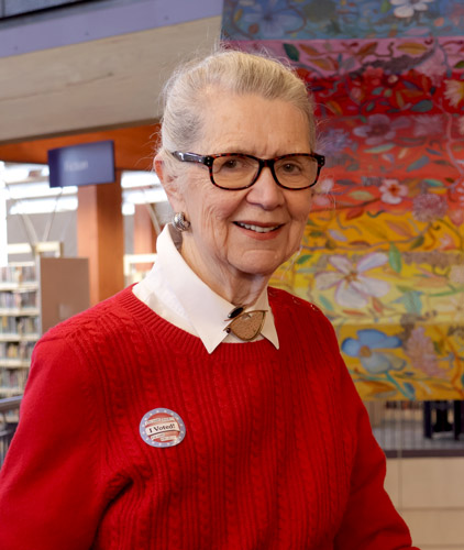 Helen Washburn stands in the Columbia Public Library with large hanging artwork and book shelves in the background