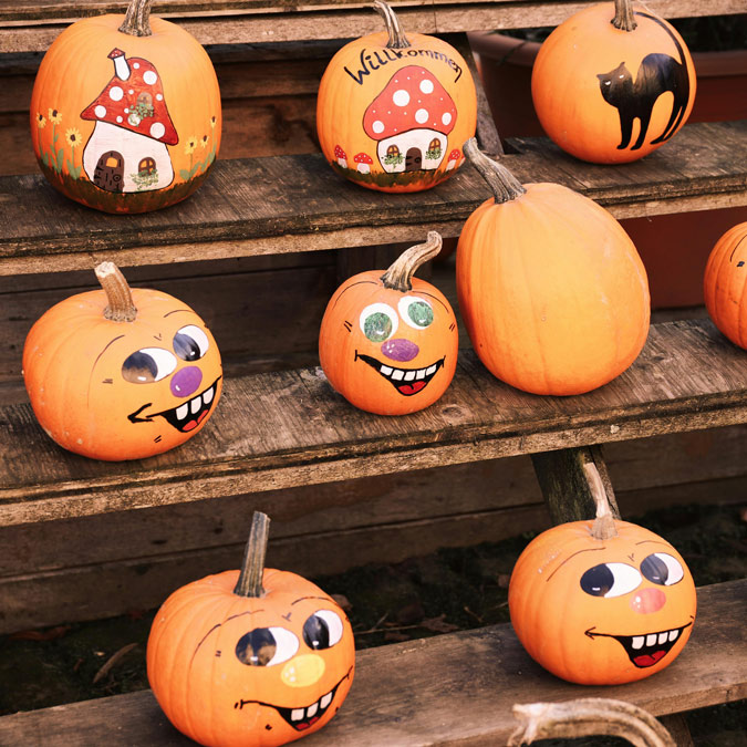 pumpkins painted with goofy faces, gnome houses and a black cat sit on wooden risers