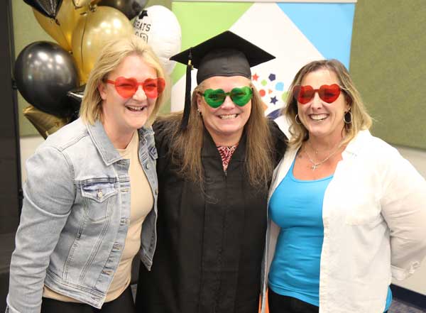 Proud graduate in cap and gown with smiling supporters on each side.