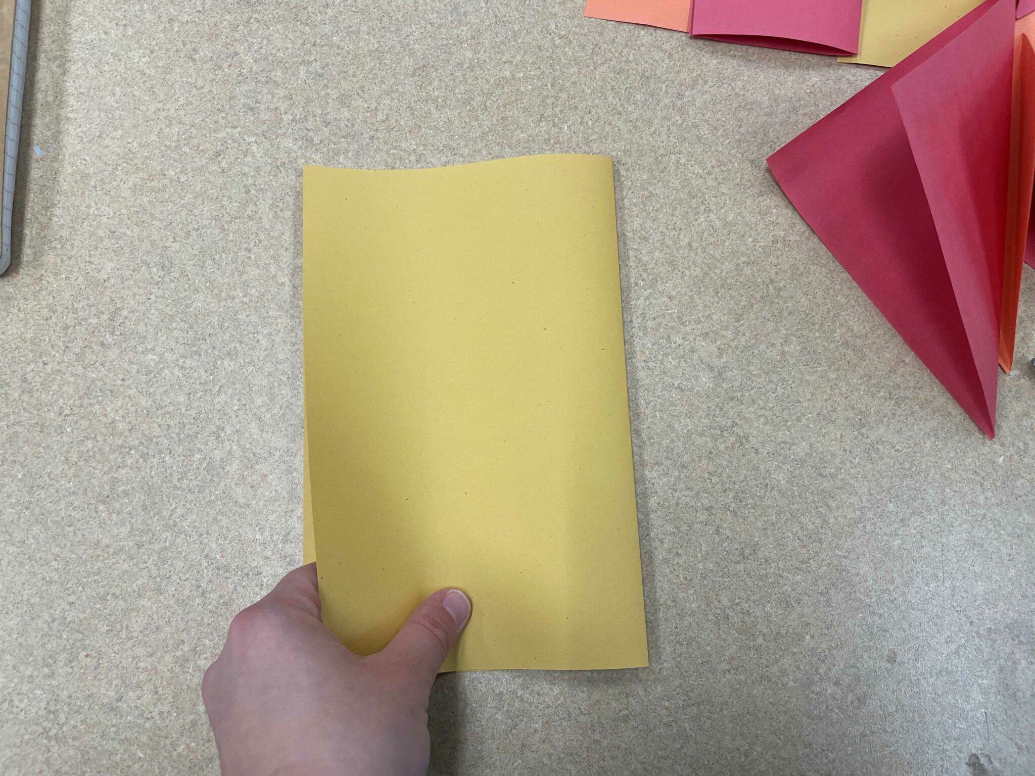A white hand holding a folded piece of yellow paper, to illustrate a "hamburger style" fold. 