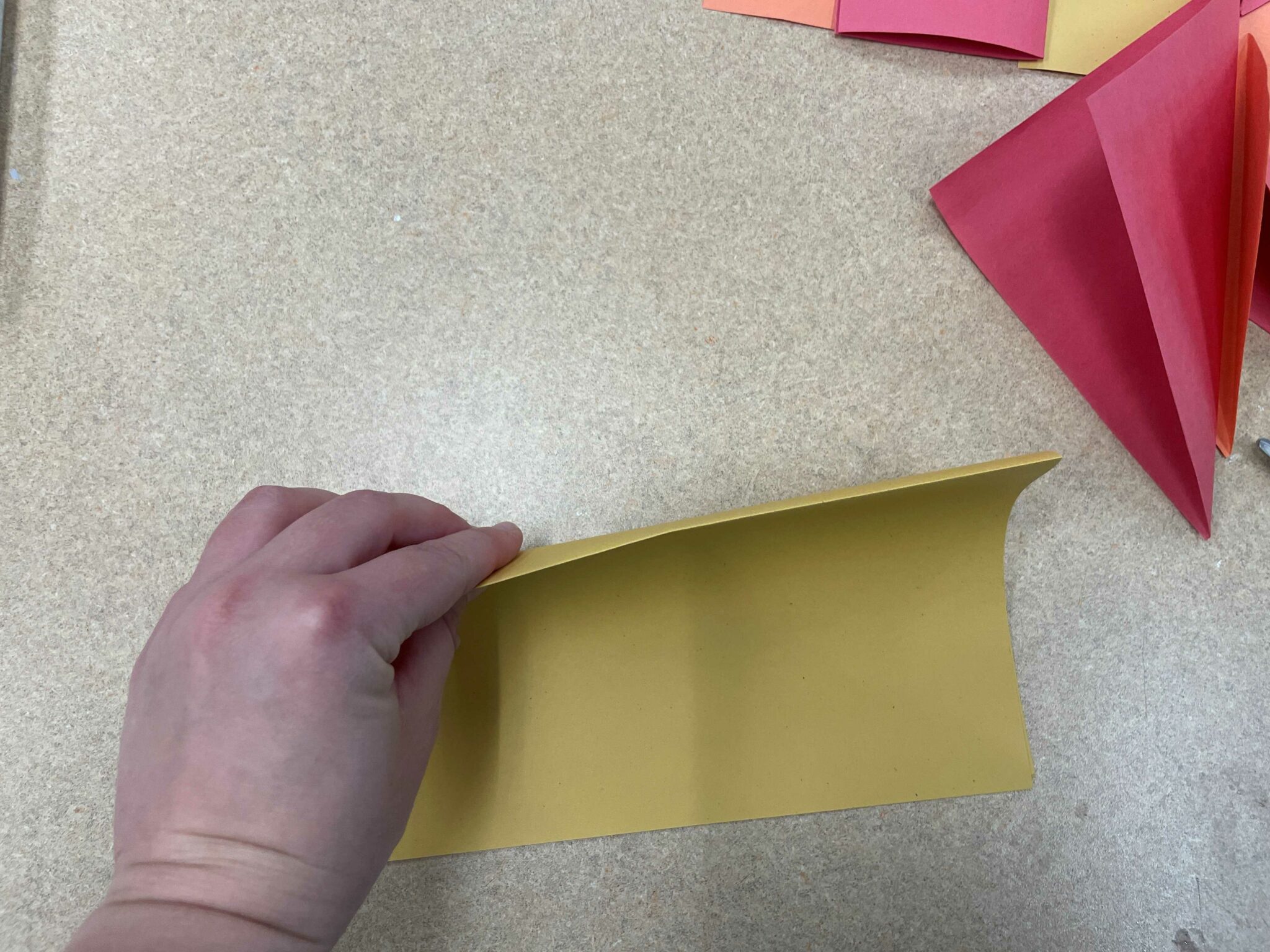 A white hand holds up a folded piece of yellow paper, to illustrate the fold in the center of the paper. 