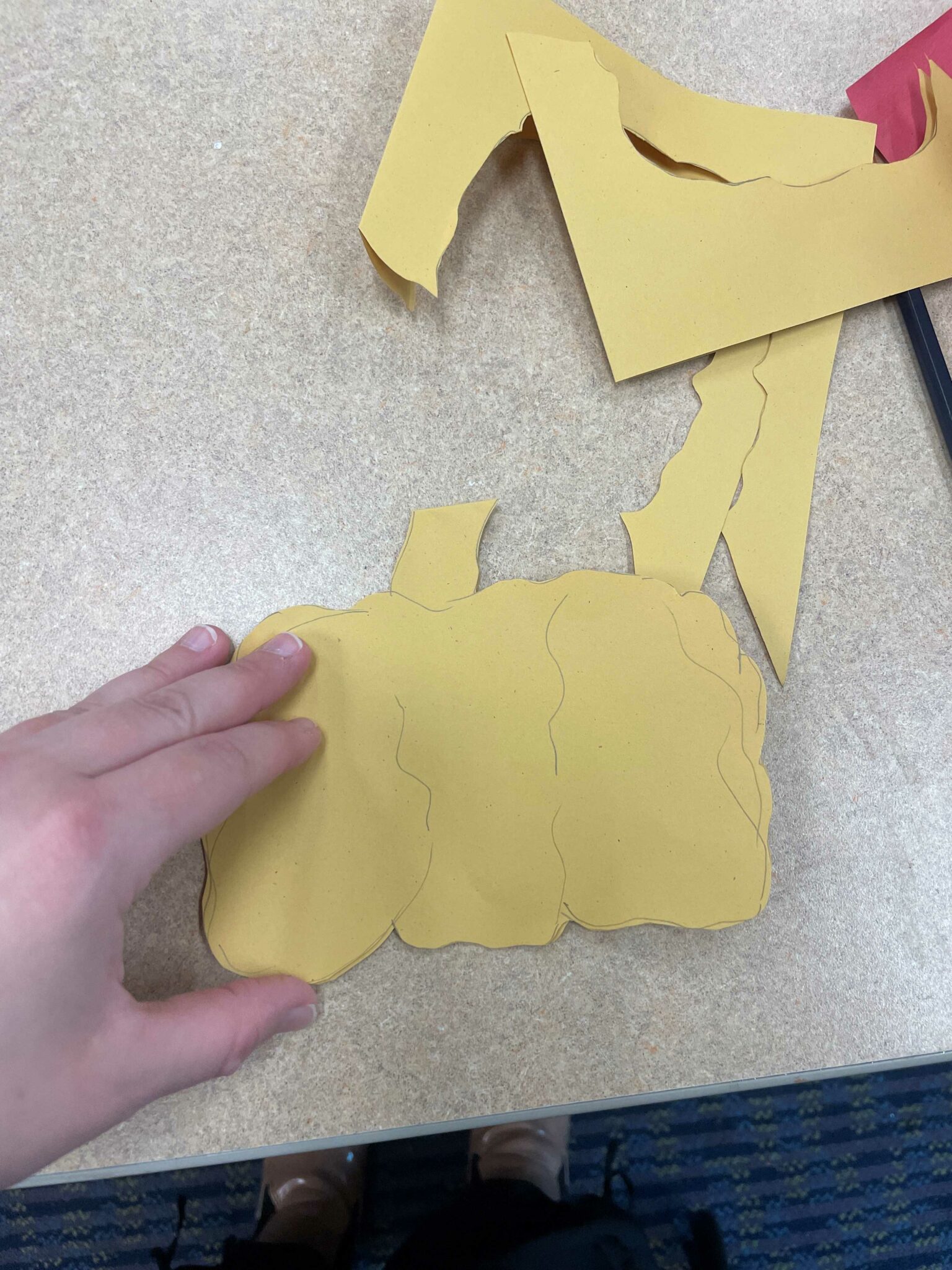 A white hand displays a large yellow pumpkin cutout of a yellow half sheet of paper. 