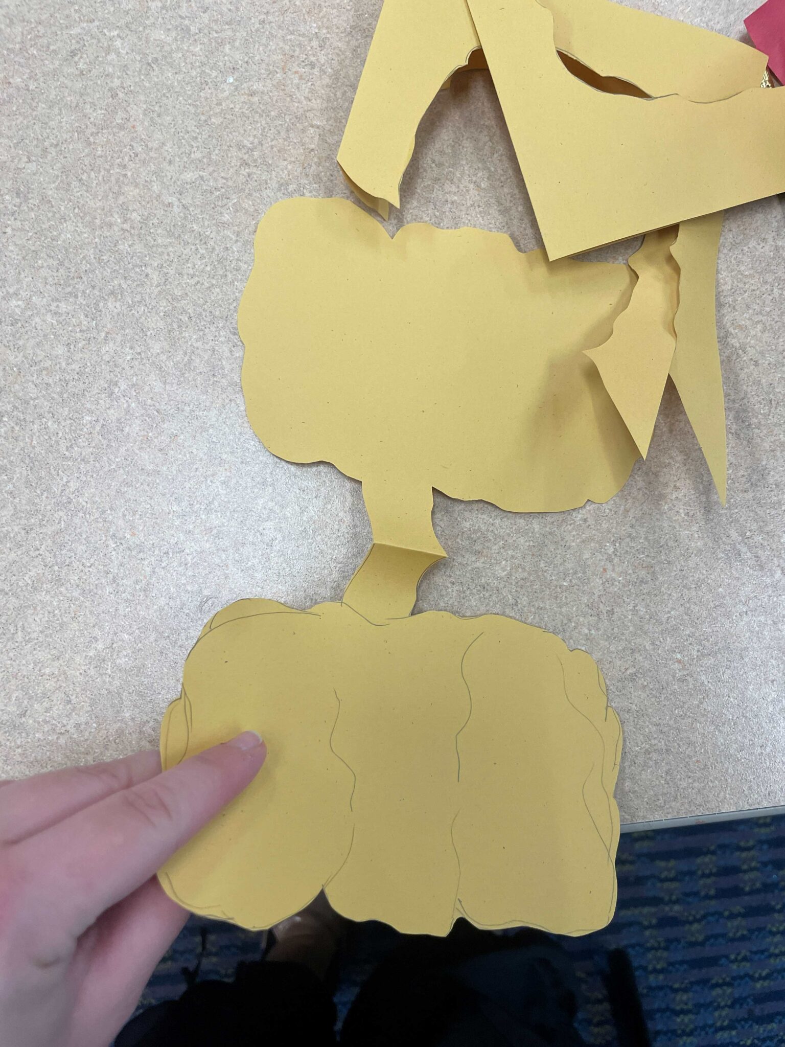 A white hand has unfolded a paper cutout of a larger yellow pumpkin shape, to illustrate how the shape is mirrored over this fold. 