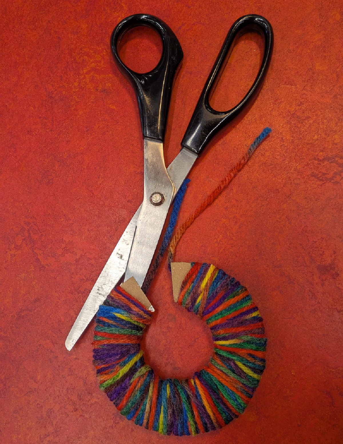 Scissors cutting the edge of the string wrapped around the cardboard 'c'