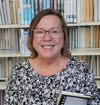 portrait of Tonya Hays-Martin standing in front of library book shelves and holding a book