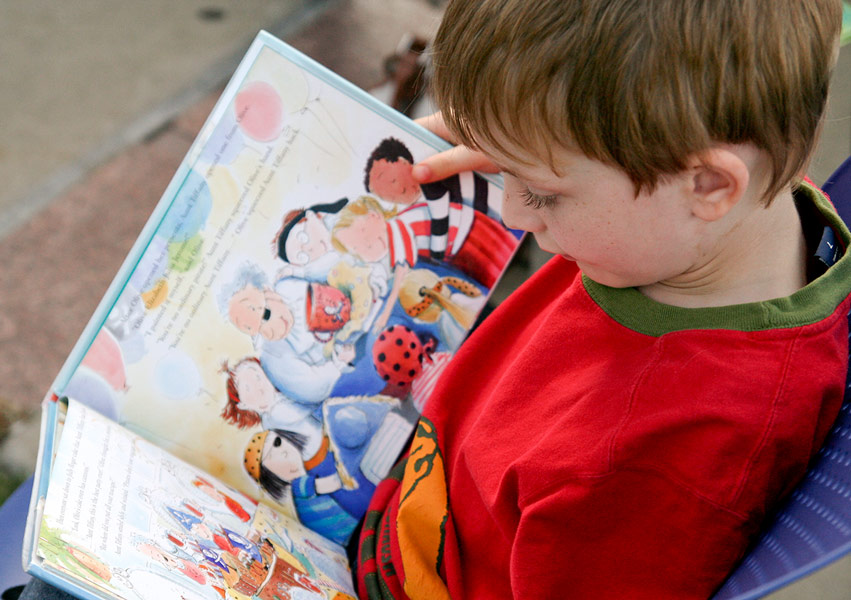 A seated young child looks down at a picture book in his lap.