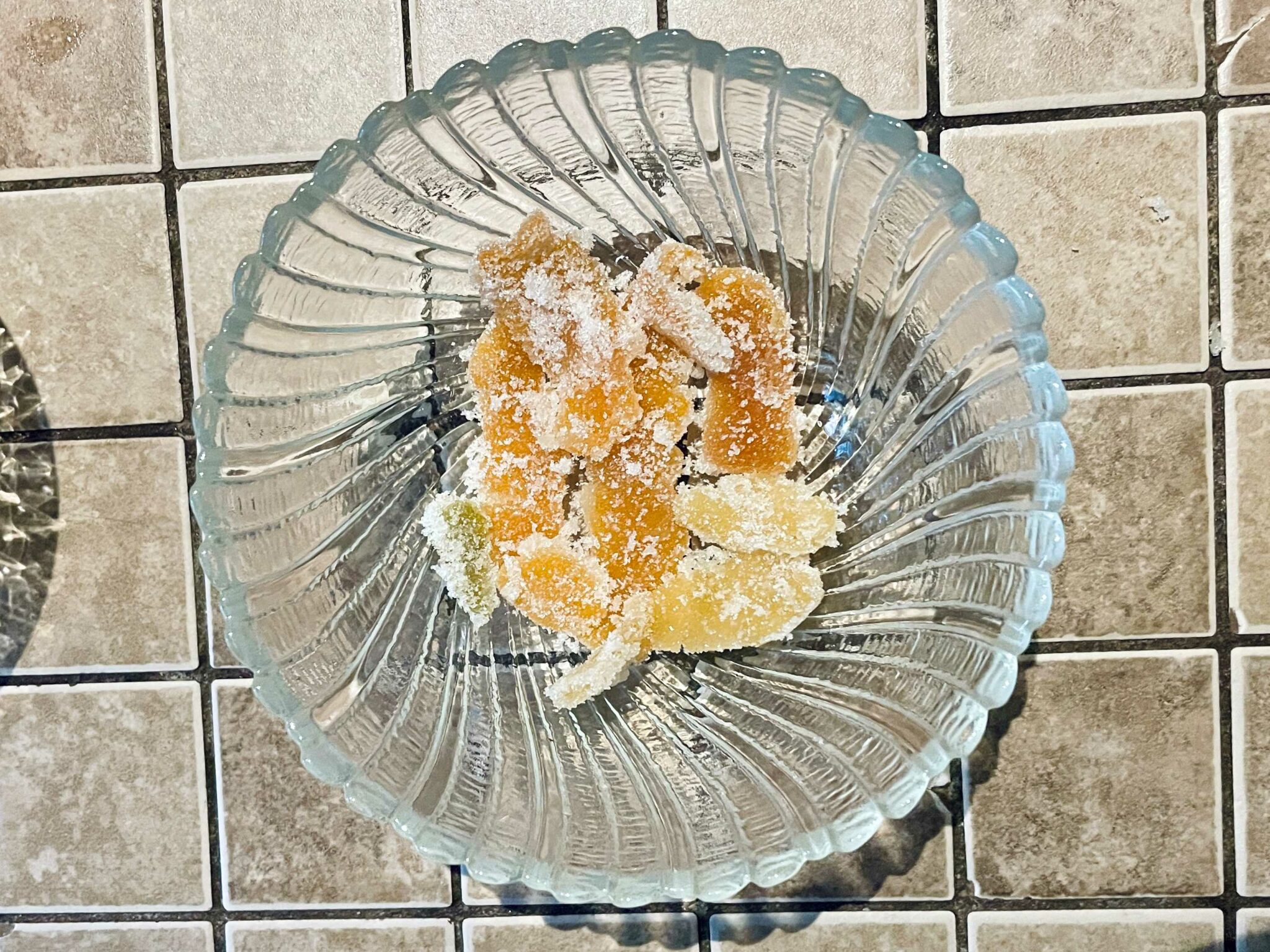 A small glass bowl with candied citrus peel inside. The variously sized peels have been rolled in sugar, so have a white crystal coating.