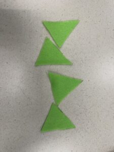 An overhead shot showing the progression of the craft project. Four individual triangular pieces of bright green felt, freshly cut from a template.