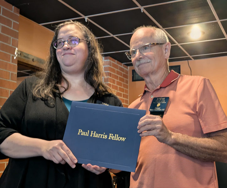 Sara Henry is presented with a certificate folder which says "Paul Harris Fellow"