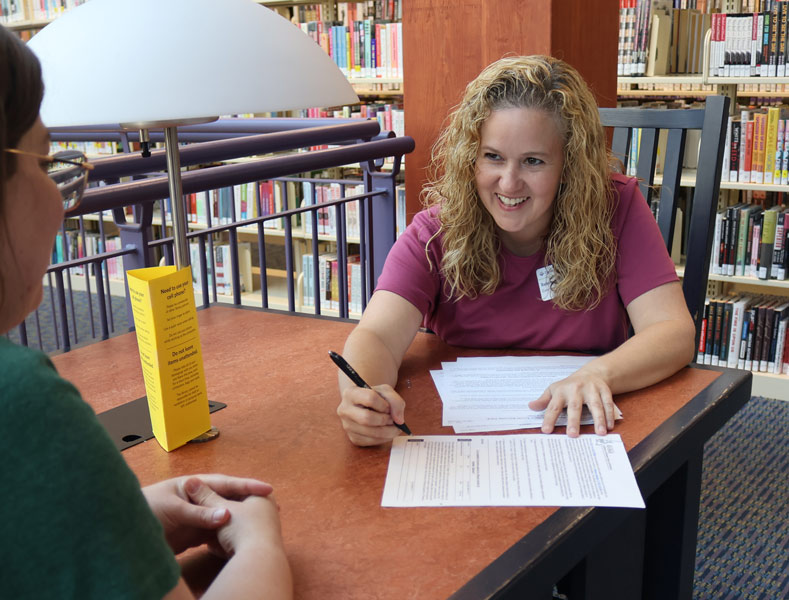 the library's social work manager sits at a library table showing a person how to fill out some paperwork