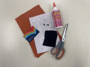 DIY card holder materials: orange, white, and black craft felt, googly eyes, felt glue, scissors, and a library card for measuring.