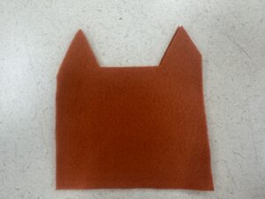The cut-out orange felt base for the DIY card holder, trimmed with pointed fox ears ready for assembly.