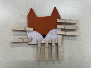 Clamping glued seams of the felt fox card holder with wooden clothespins along the sides and bottom edge to dry securely.