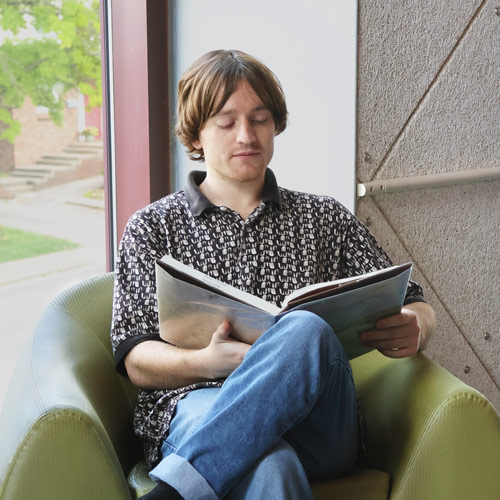 a person reading a book in a library chair by the window